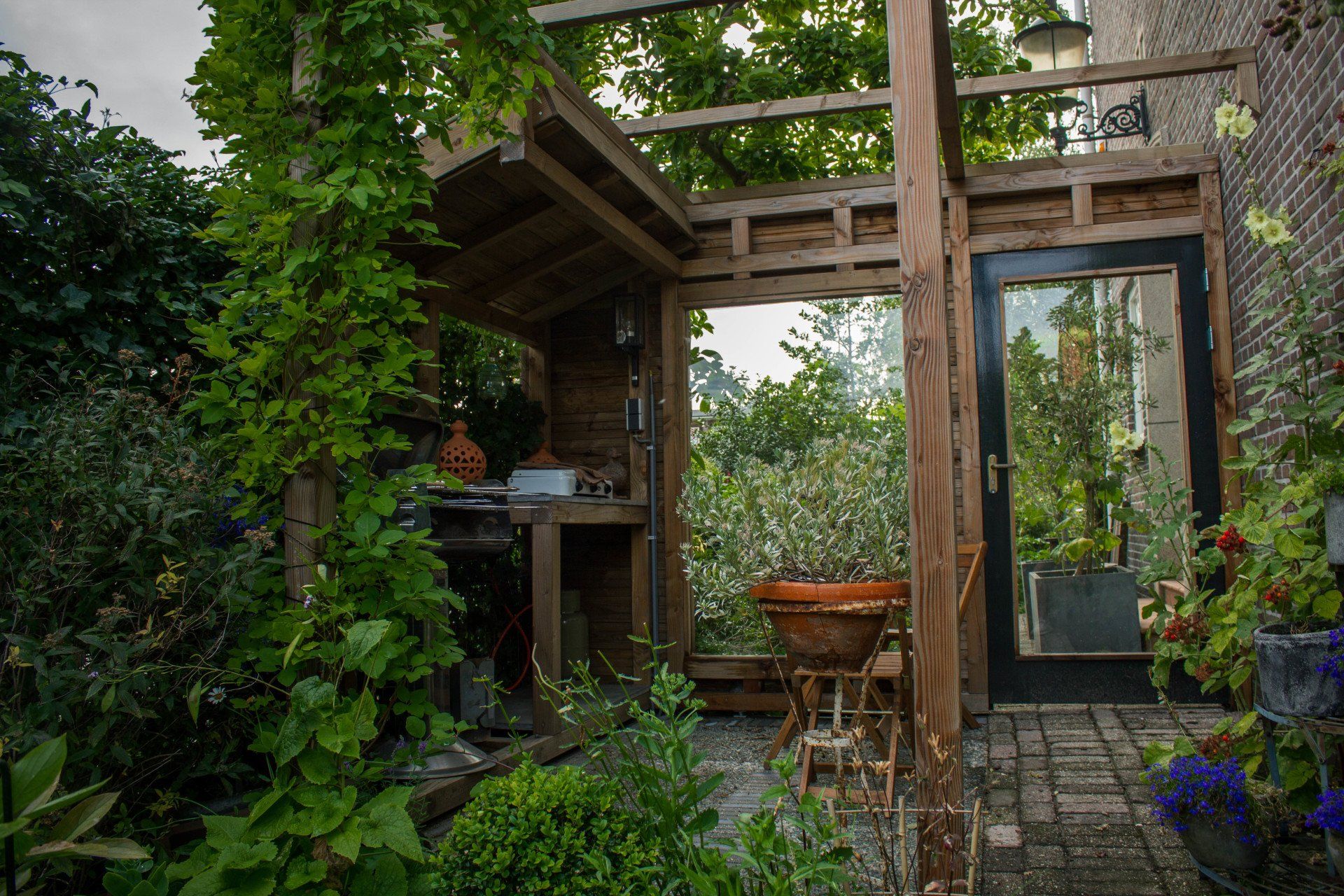 Houten buitenkeuken met deur en planten.