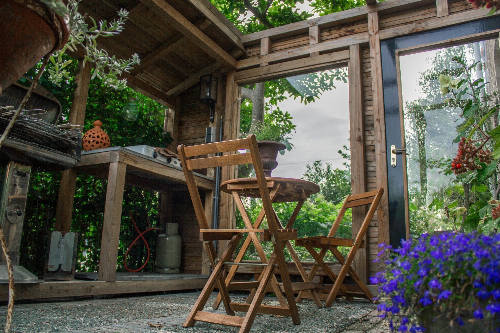 Houten zitgedeelte buiten met tafel, stoelen en omringende beplanting.