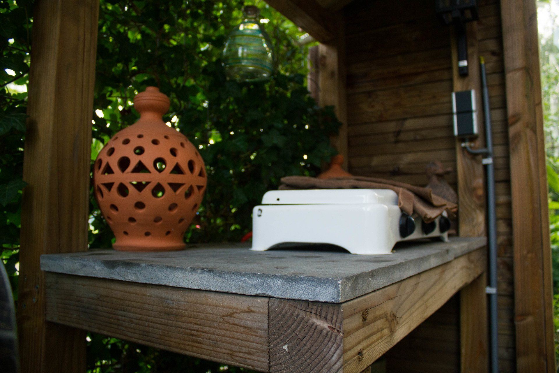 Een terracotta lantaarn en een wit apparaat staan ​​op een stenen plank in een houten constructie.