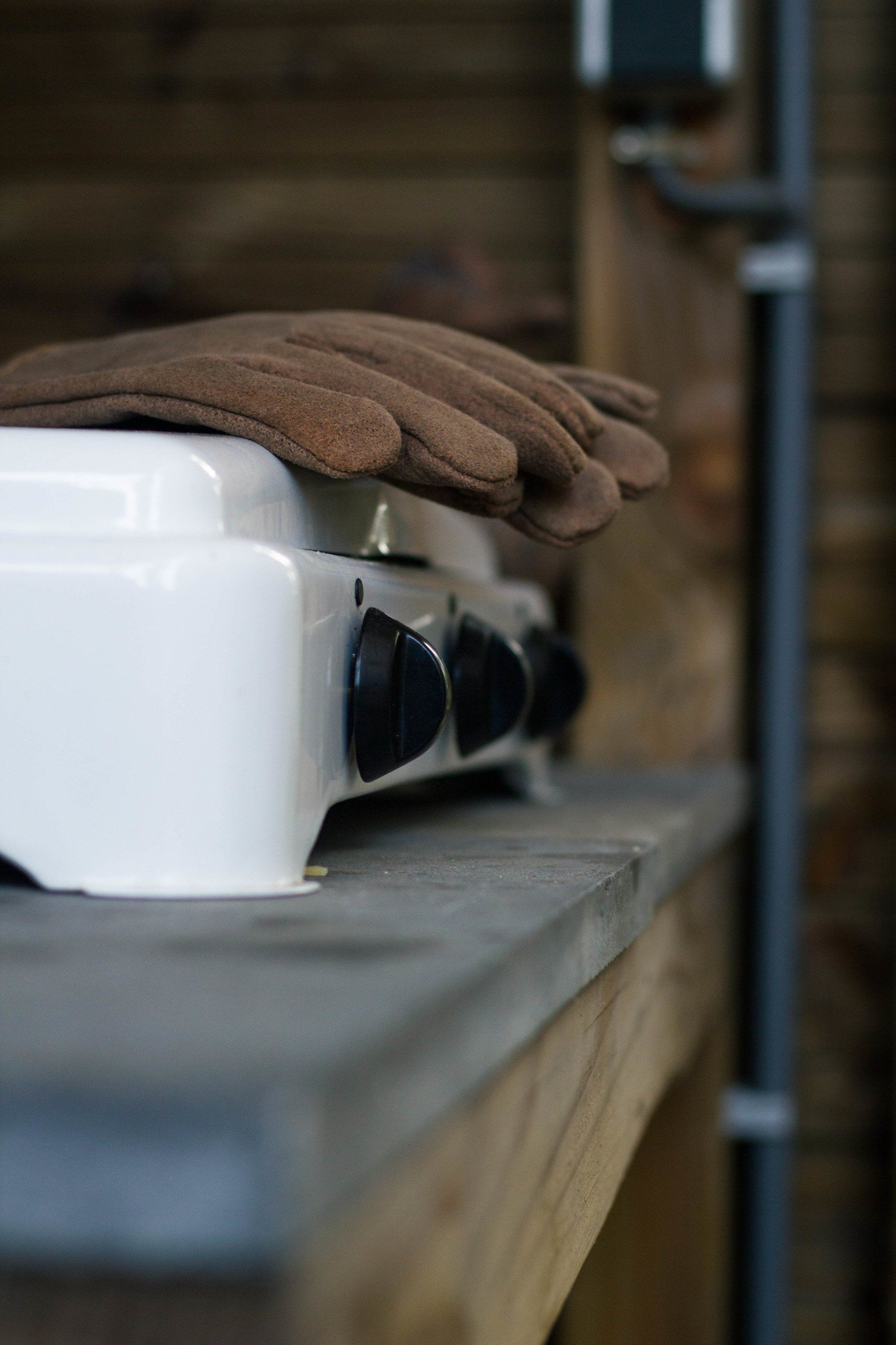 Witte elektrische kookplaat met bruine ovenwanten, op een houten plank.