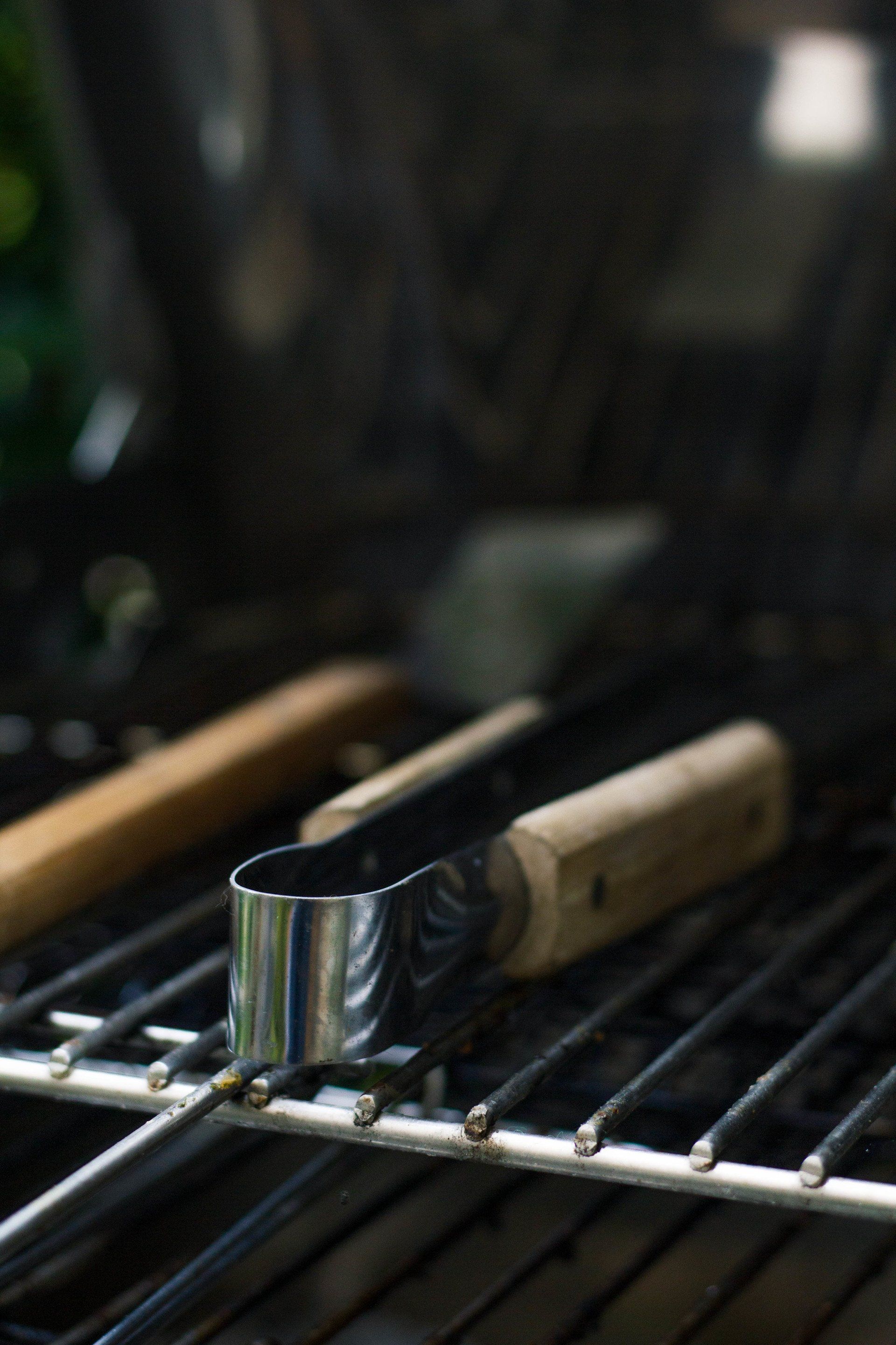 Een tang en een spatel met houten handvatten liggen op een grillrooster, mogelijk klaar om te gaan koken.