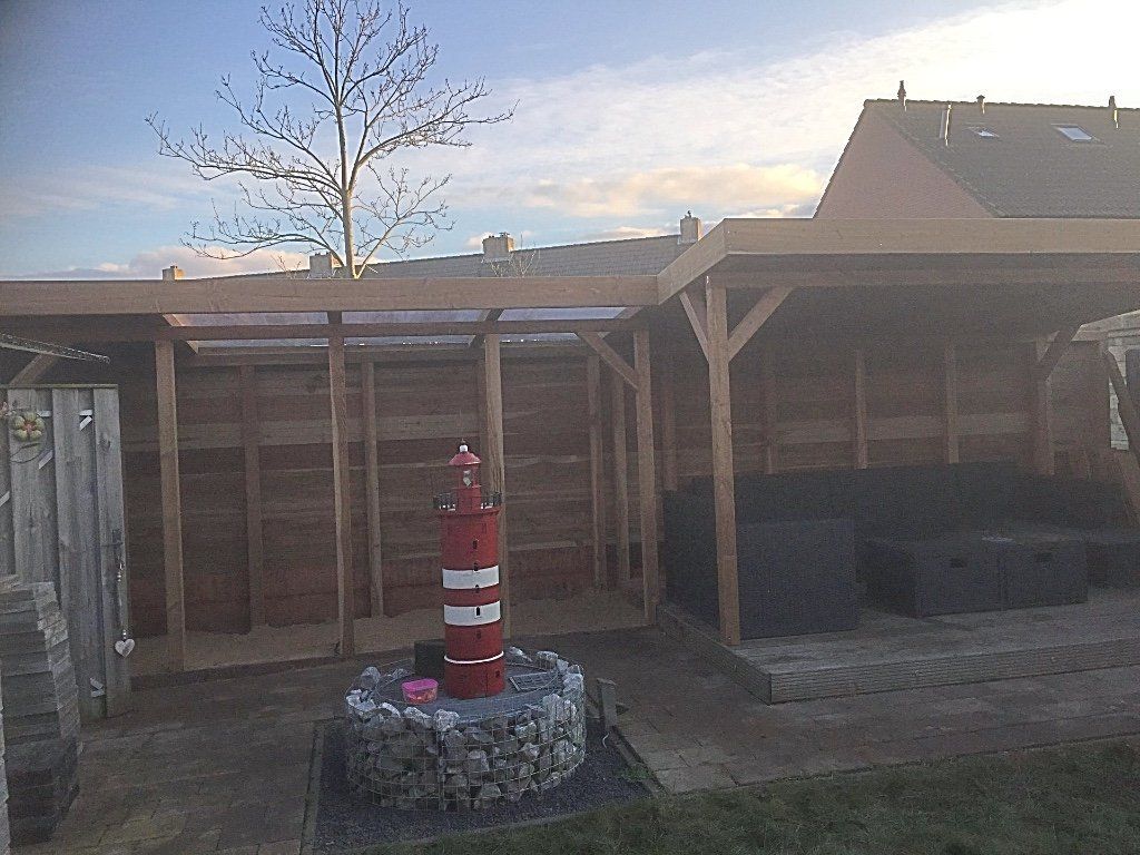 Houten buitenverblijf met zitgelegenheid, een rood-wit vuurtorenornament en een hek.