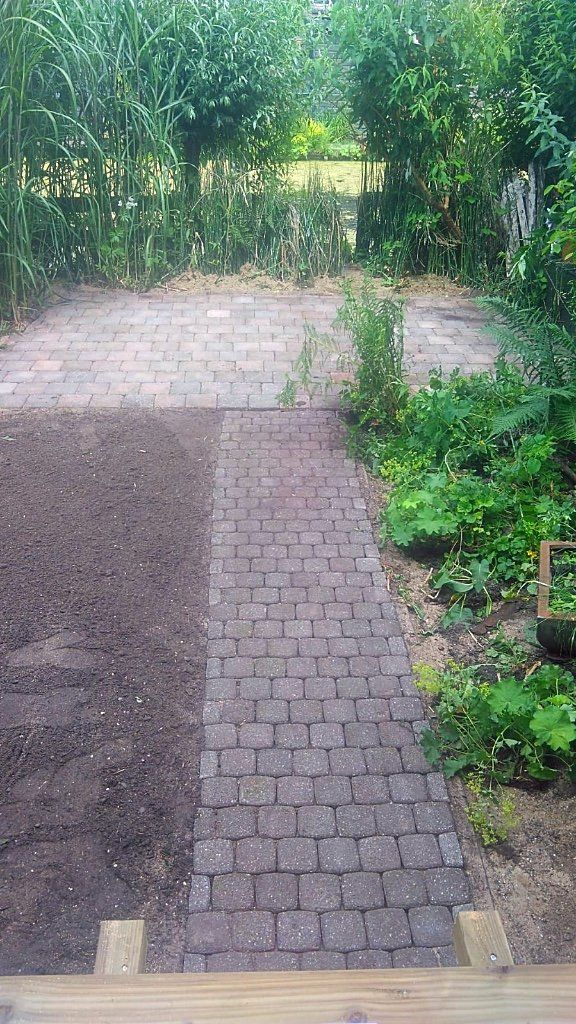 Een bakstenen pad door een tuin leidt naar een poort. Aarde aan de linkerkant, groen aan de rechterkant.