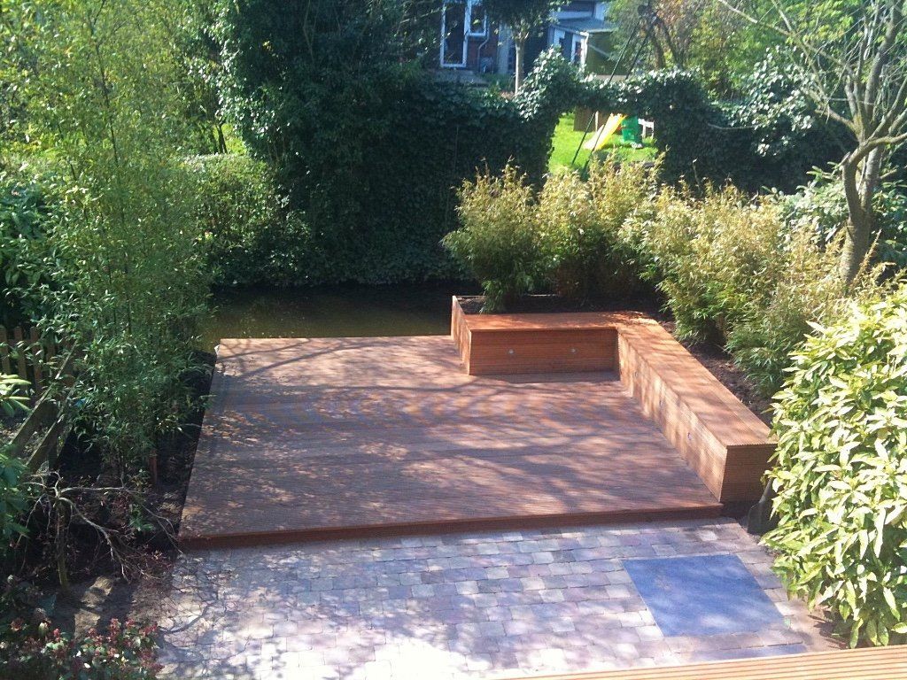 Houten terras met zitgedeelte aan een vijver, omgeven door groen.
