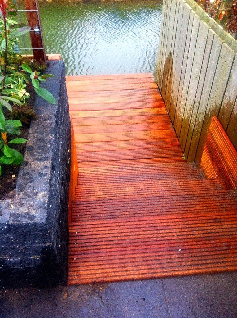 Houten traptreden die naar het water leiden, naast een plantenbak en een muur.