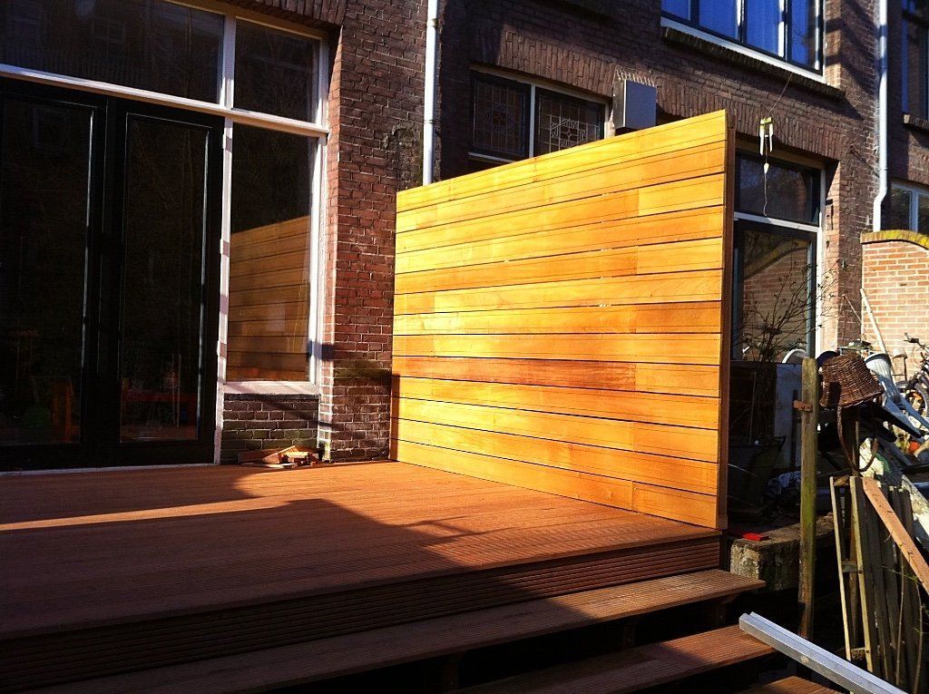 Houten privacyscherm op een terras naast een bakstenen gebouw met een trap.
