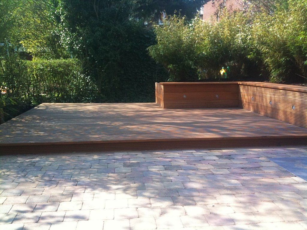 Houten terras met plantenbak, bakstenen patio en weelderig groen op de achtergrond.