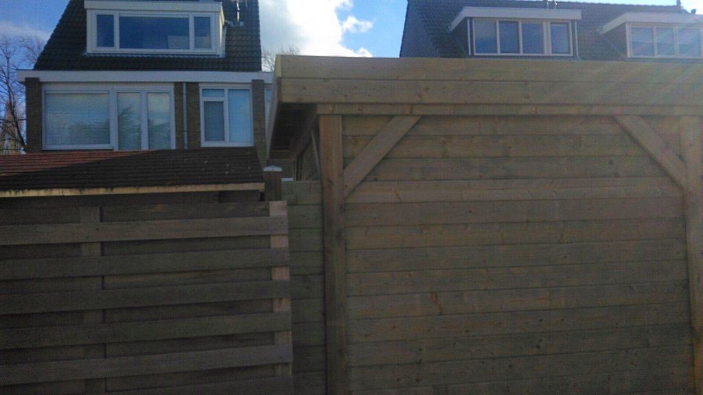 Houten hek met een poort, huizen op de achtergrond, blauwe lucht.