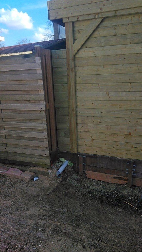 Houten schutting met horizontale planken, gebouwd naast een constructie. Aarde en lucht zichtbaar.