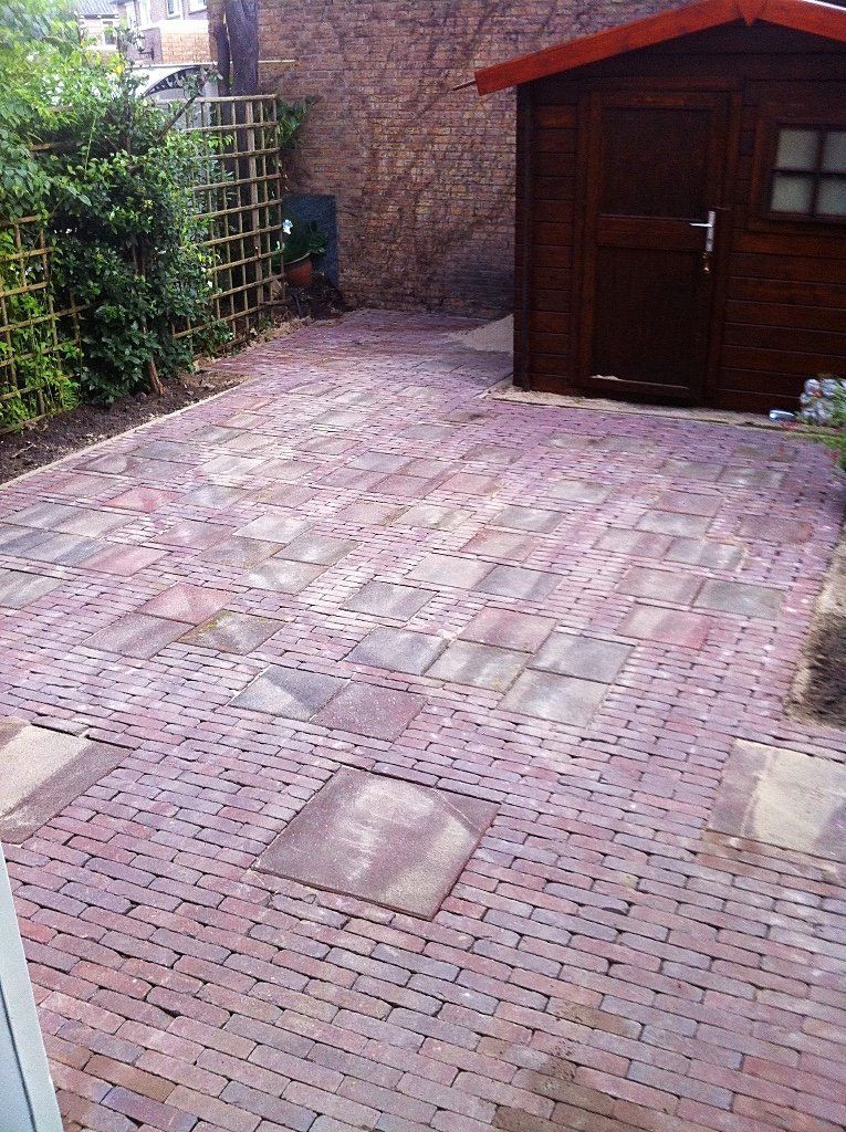 Achtertuin met bakstenen bestrating, schuur en pergola.