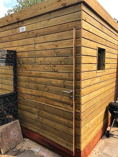 Houten schuur met horizontale planken als gevelbekleding, een deur en een klein raam, buiten geplaatst.
