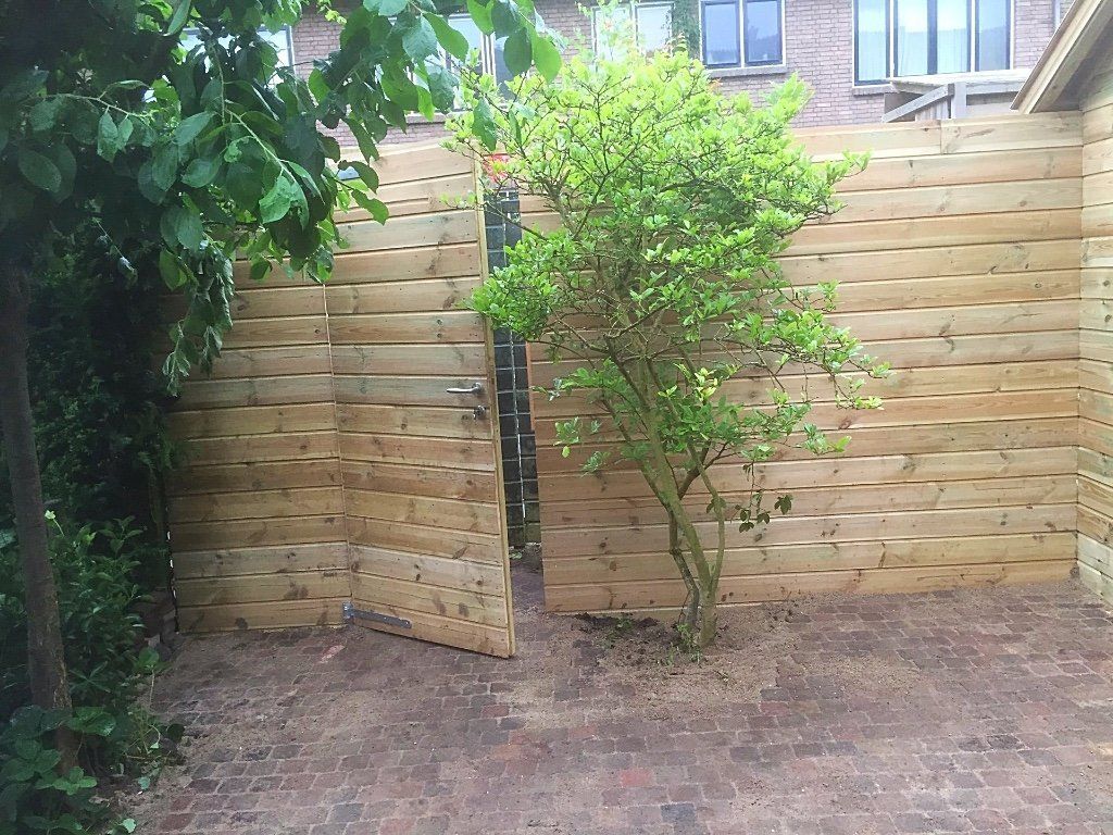 Houten schutting met een kleine boom ervoor, op een stenen terras.