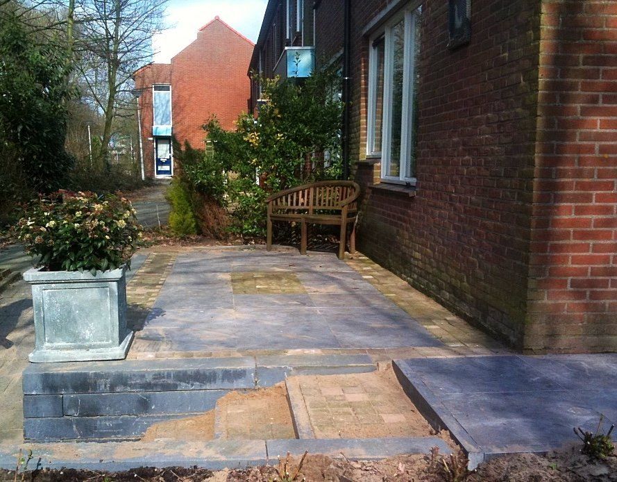 Ingang van een bakstenen gebouw met terras, bankje en potplant.