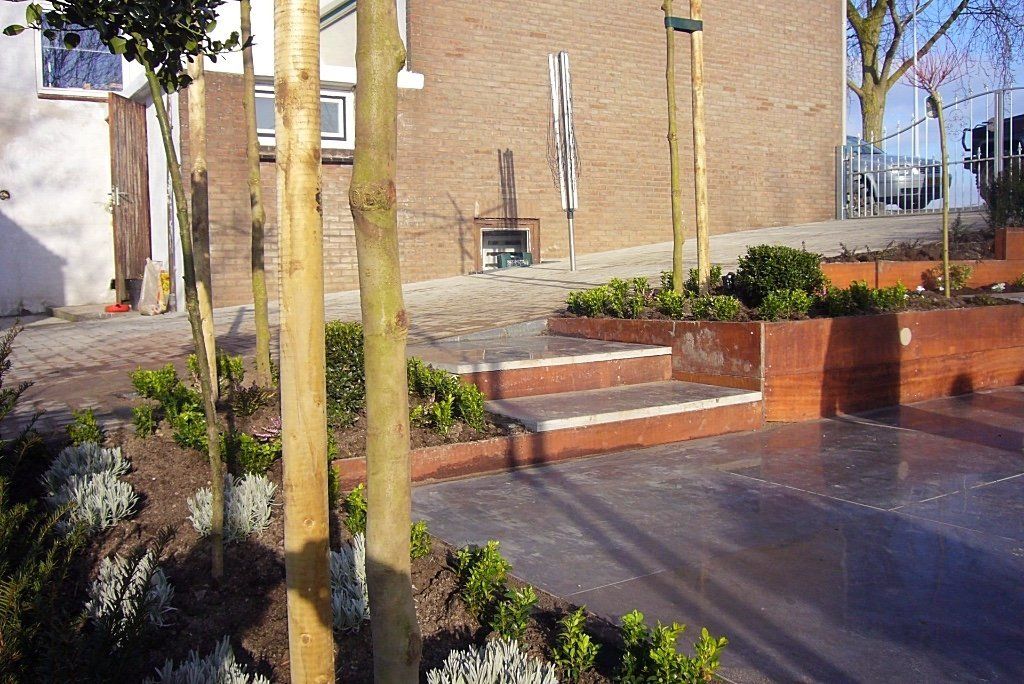 Een trap leidt naar een tuin met plantenbakken in verschillende niveaus, gevuld met struiken en jonge bomen.