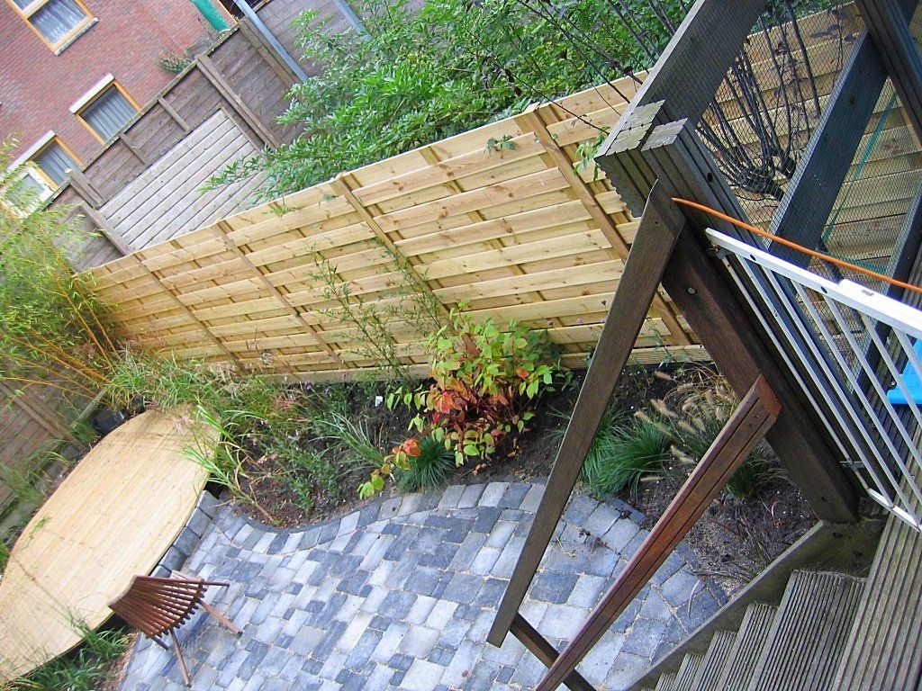 Terras in de achtertuin met houten schutting, stenen bijgebouw en trap.
