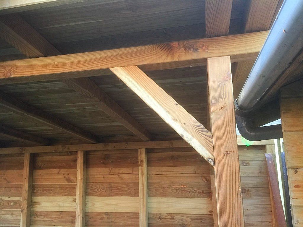 Houten constructie met draagbalken en een dak, zichtbaar vanaf de onderkant. Inclusief dakgoot.