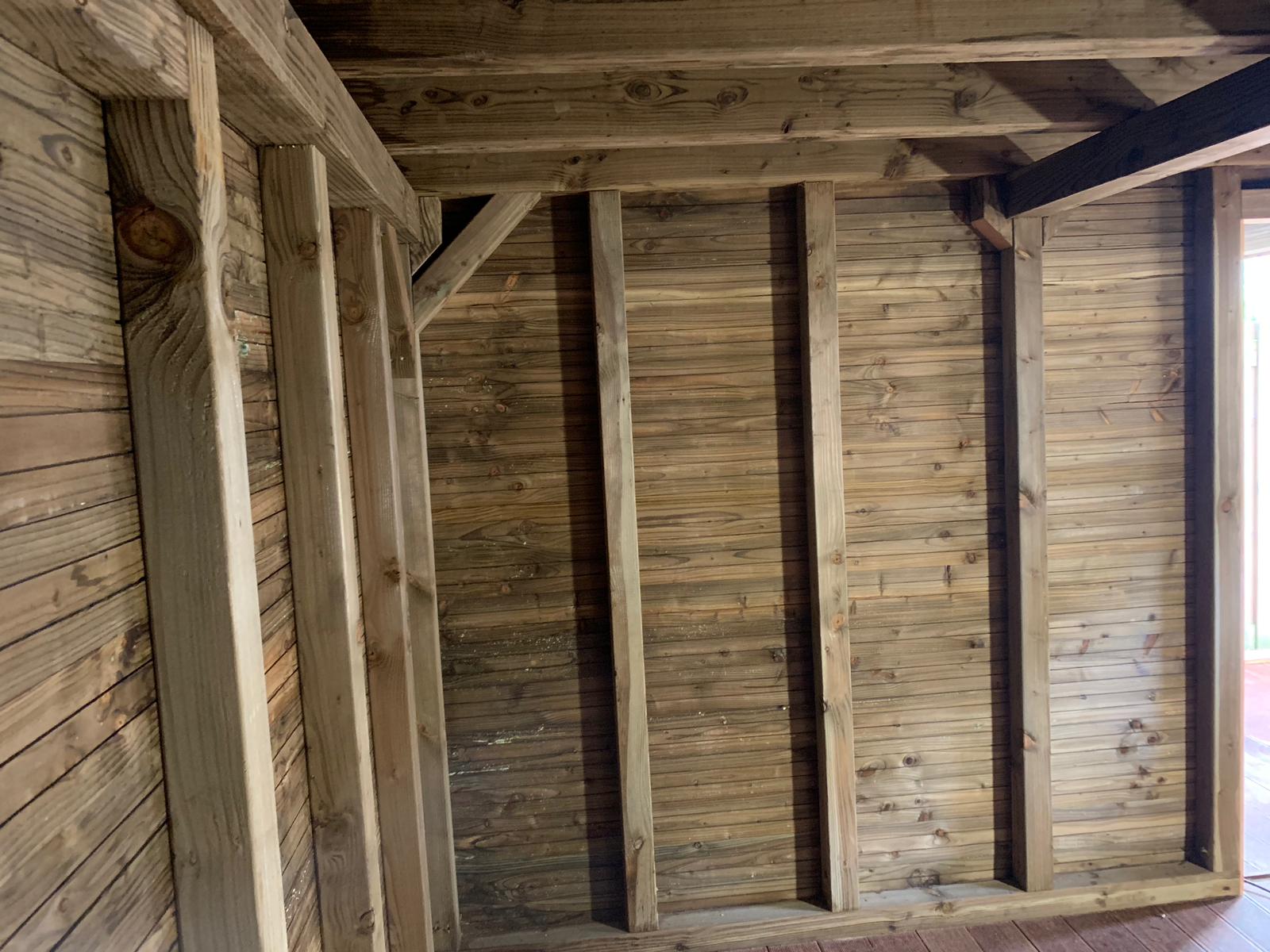 Interieur van een houten constructie, met zichtbare balken en verticale houten lambrisering op de wanden.