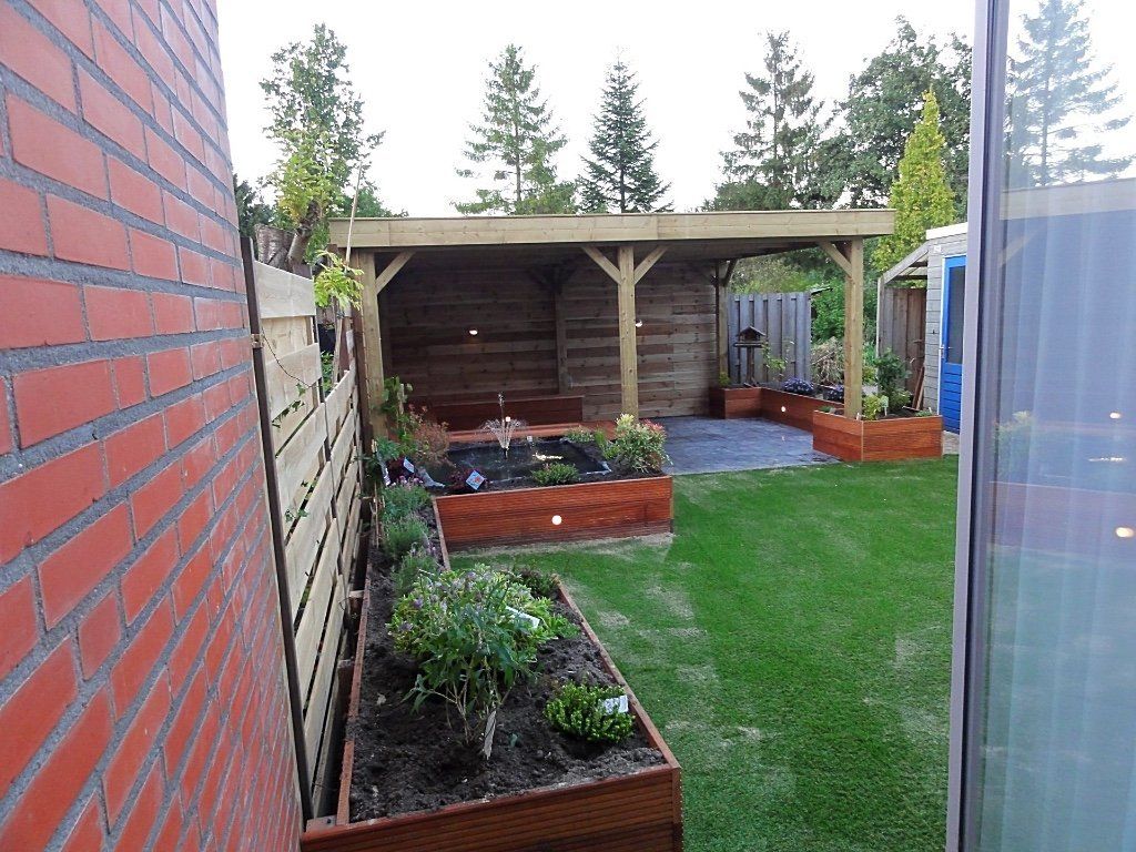 Achtertuin met een houten pergola, verhoogde bloembedden, een groen gazon en een bakstenen muur.