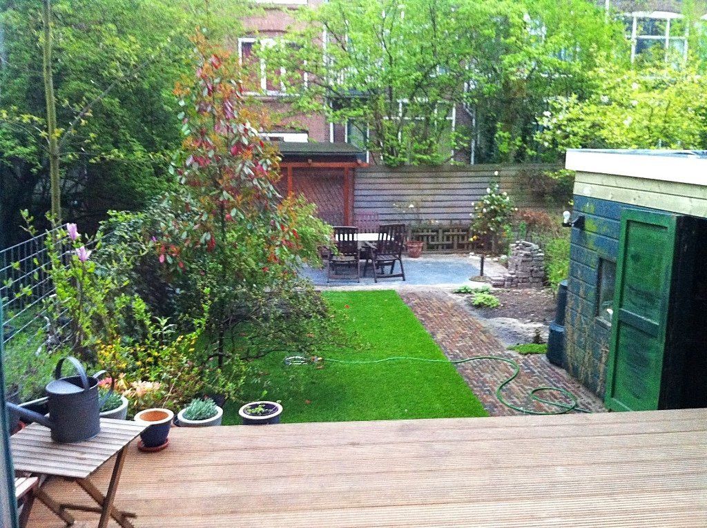 Achtertuin met groen gras, bomen, schuur en tuinmeubilair.