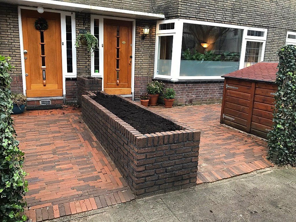 Een bakstenen gevel met bruine deuren, een bakstenen plantenbak en een klein hondenhok.