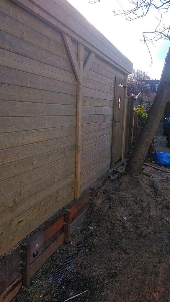 Houten schuur met een deur en een boom ernaast.