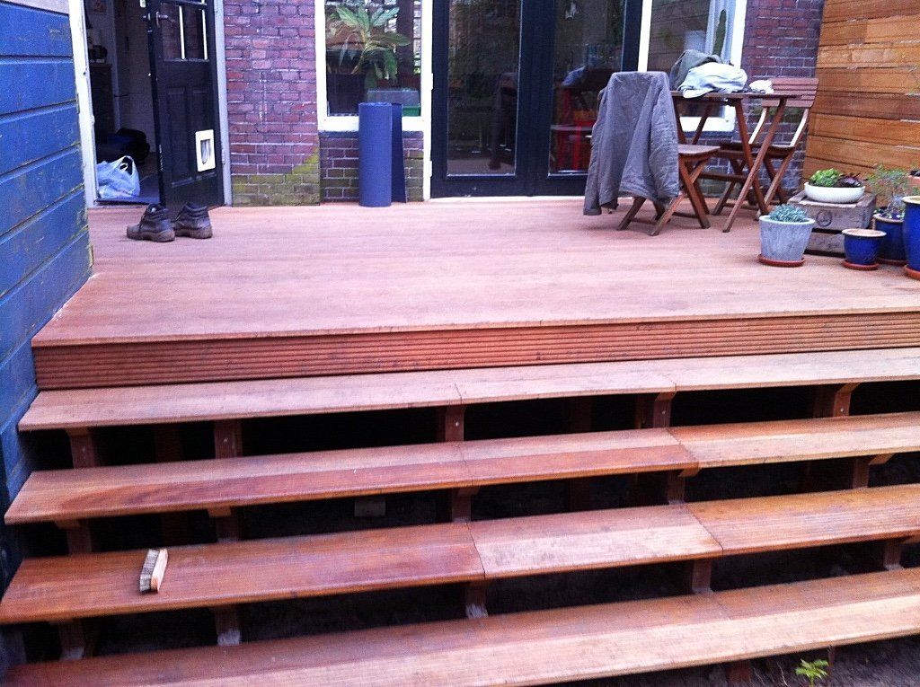 Houten terras met drie treden die leiden naar een verhoogd platform vlakbij een huis.
