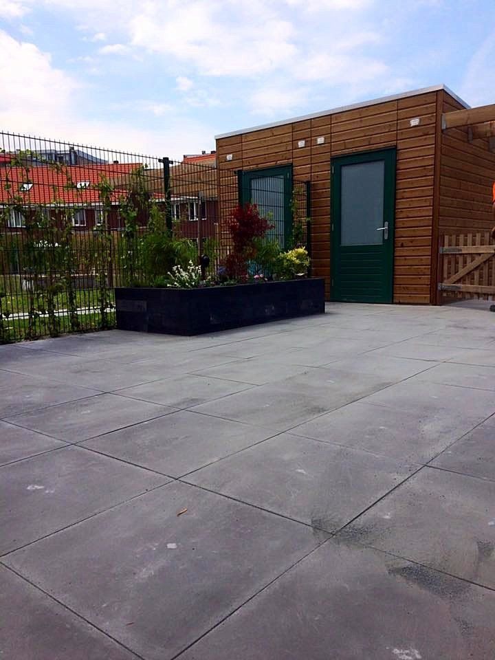 Terras met een houten bijgebouw, groene deuren en een rechthoekige plantenbak.