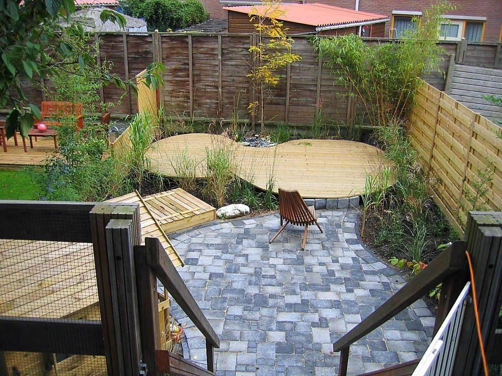 Een klein terras in de achtertuin met een stenen pad, houten vlonders en diverse planten.