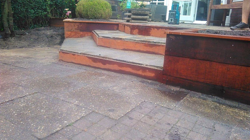 Roestige metalen keermuur met trappen, op een terras.