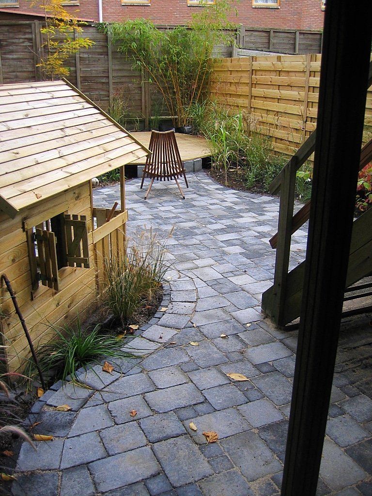 Een stenen terras met een houten speelhuisje, een stoel en een schutting in de achtertuin.