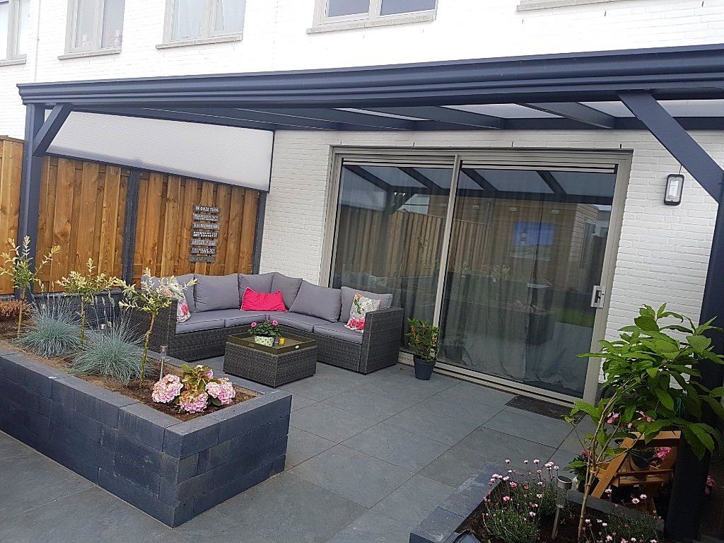 Terras met grijs meubilair, een pergola en potplanten naast een huis met een schuifdeur van glas.