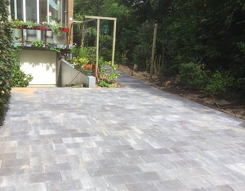 Een met bestrating aangelegde oprit leidt naar een gebouw met een verhoogde tuin.