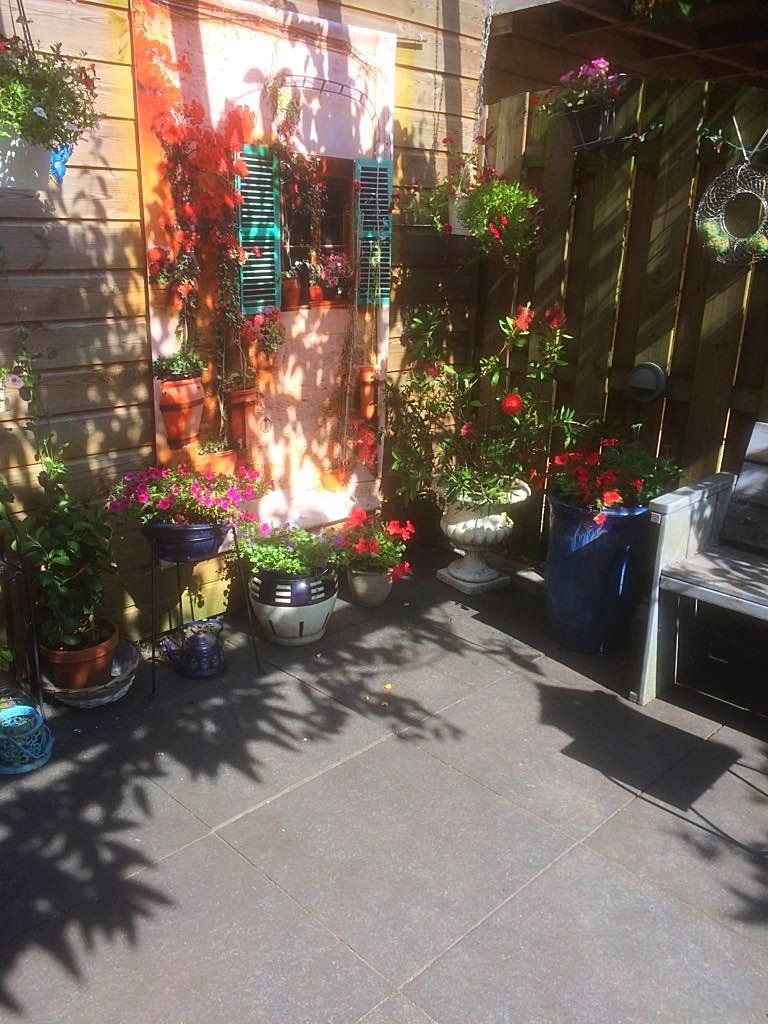 Kleurrijk terras met bloempotten, een sierlijke deur en een houten schutting die schaduwen werpt.