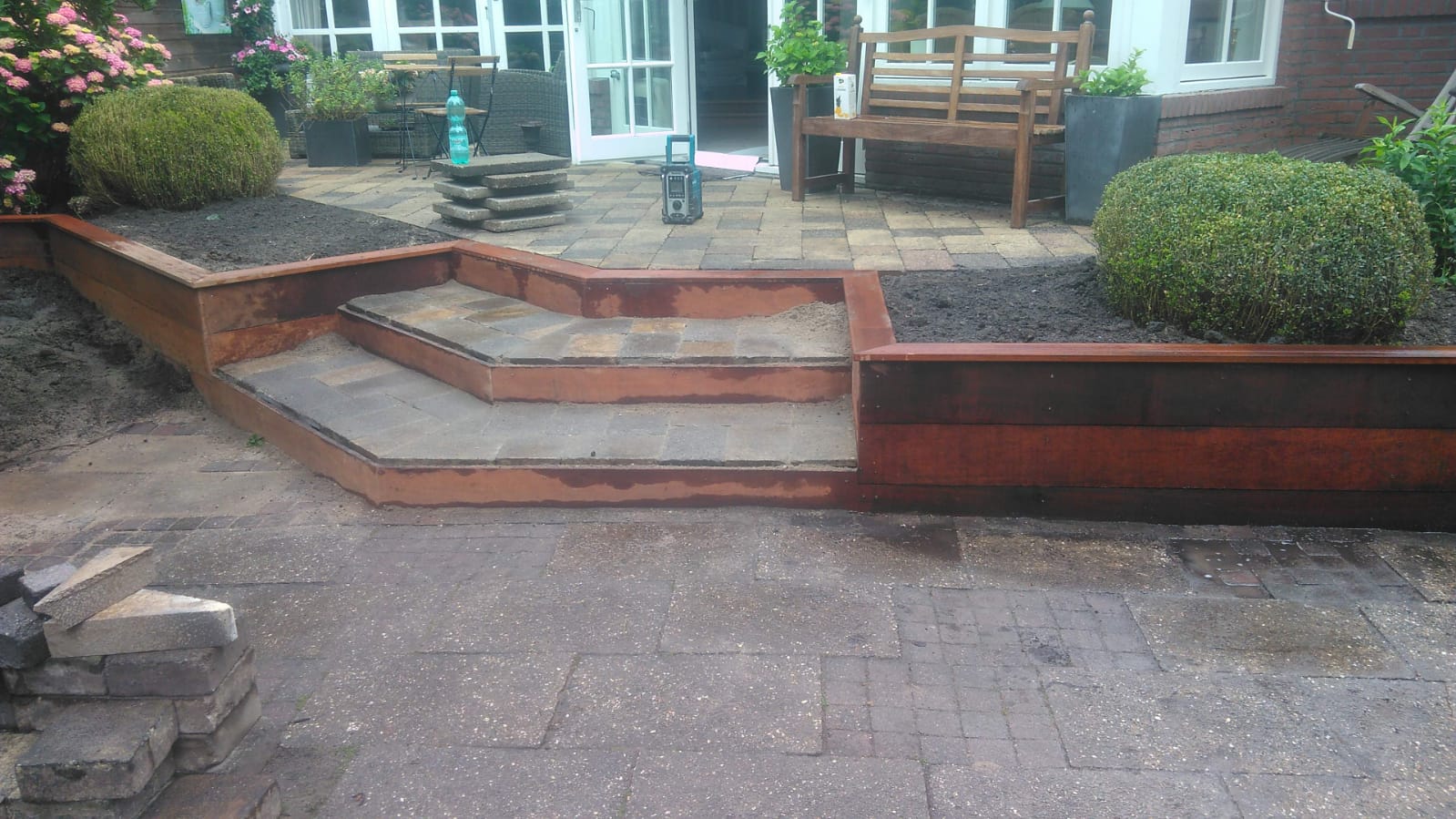Houten trappen en plantenbakken met keurig gesnoeide struiken op een betegeld terras.