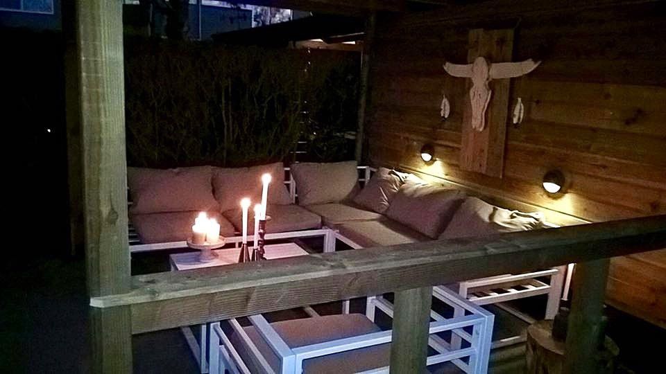 Een terras met zitgelegenheid 's avonds, verlicht met kaarsen en houten accenten.