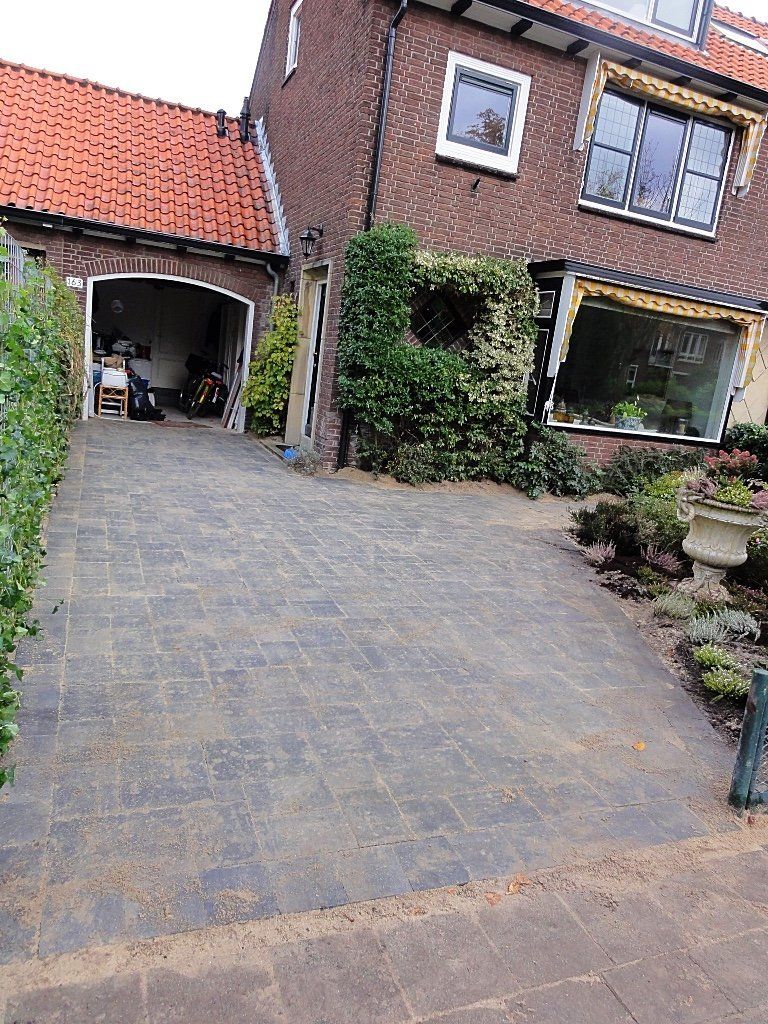 Oprit die leidt naar een bakstenen huis met een garage en omgeven door groen.