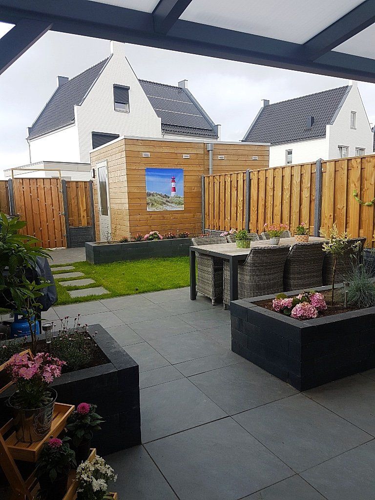 Terras met tafel, planten en houten schutting, grenzend aan een gazon met huizen op de achtergrond.