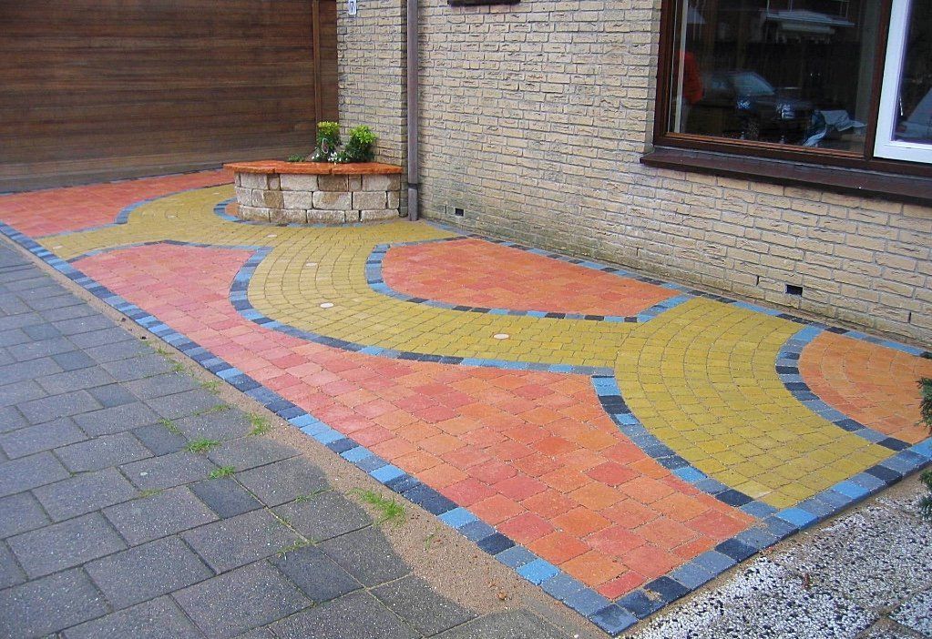 Een terras van veelkleurige bakstenen met een gebogen ontwerp naast een bakstenen gebouw; accenten in oranje, geel en blauw.