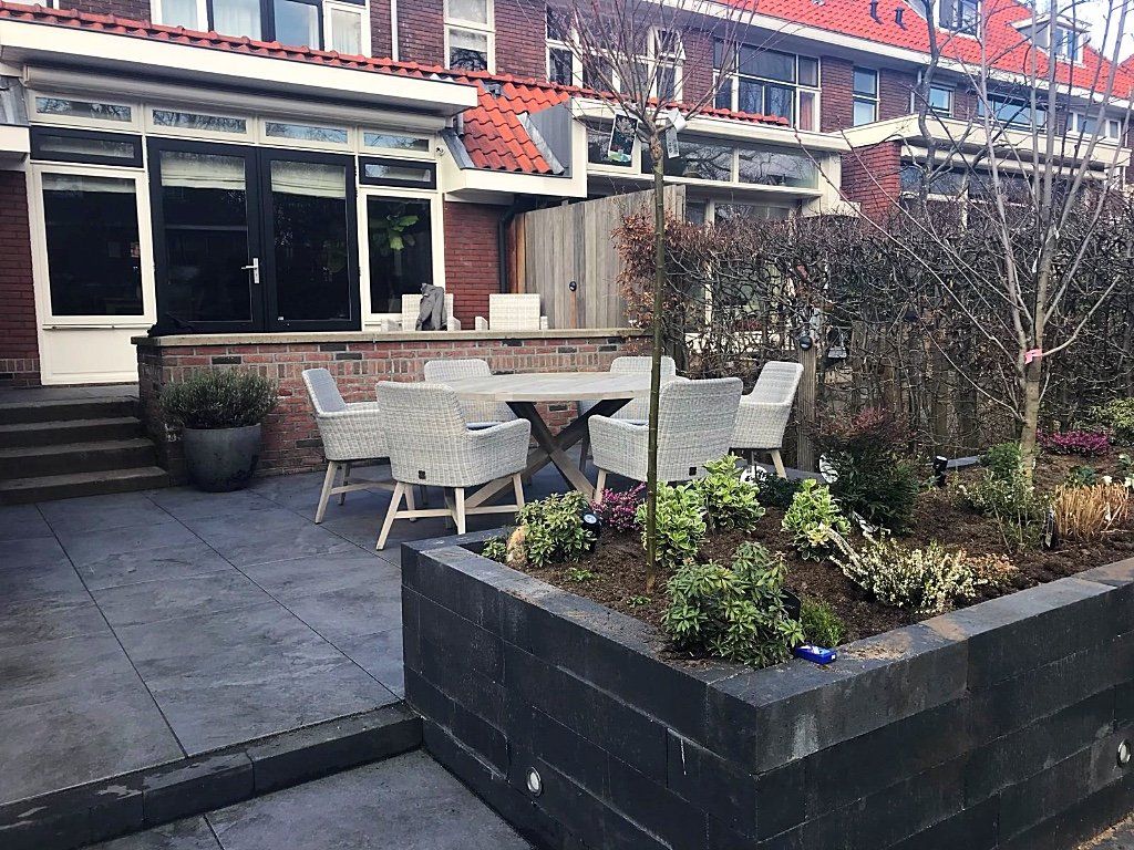 Terras met een tafel en stoelen, omgeven door een verhoogd bloembed en bakstenen gebouwen.