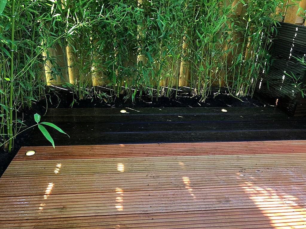 Houten terras met bamboeplanten op de achtergrond; een donkere mulchlaag als ondergrond.
