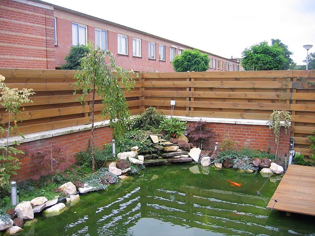 Vijver in de achtertuin met waterval, omgeven door een bakstenen en houten schutting.