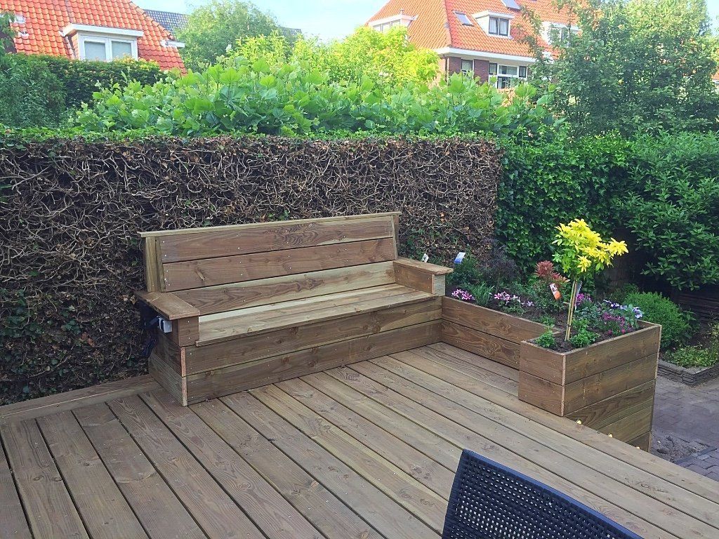 Houten bank en plantenbakken op een houten terras, met een groene heg op de achtergrond.