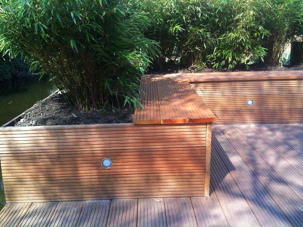 Houten plantenbakken met bamboeplanten naast een houten terras, gedeeltelijk verlicht door de zon.