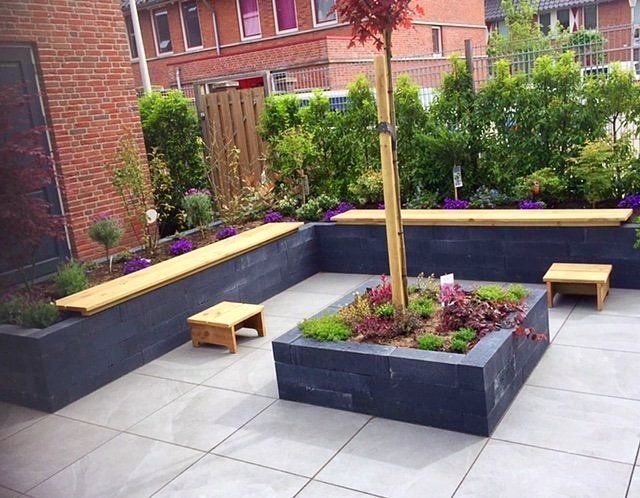 Een modern terras met ingebouwde banken, een centrale plantenbak en omringende beplanting.