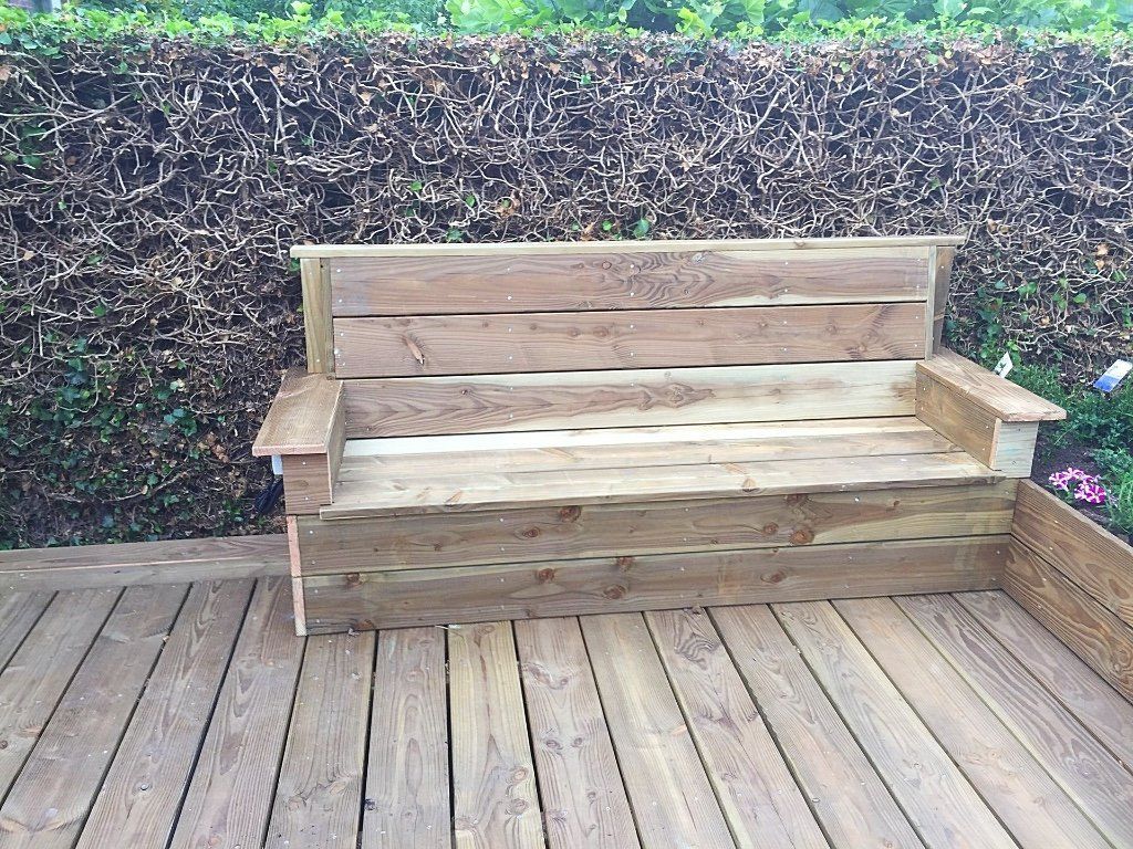 Houten bank op een houten terras voor een heg.