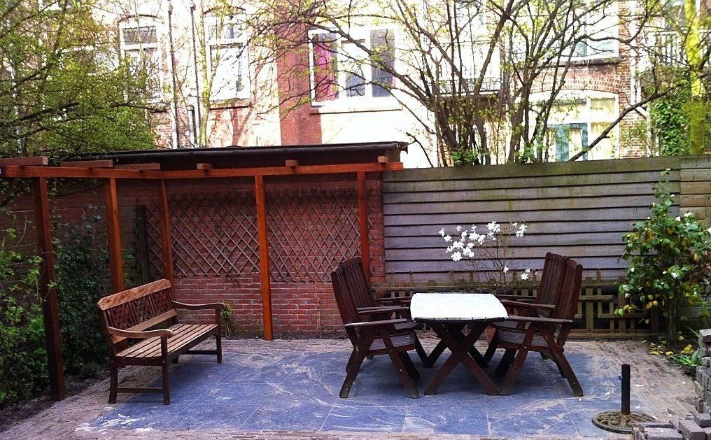 Buitenpatio met houten meubilair onder een afdak en een tafel met stoelen.