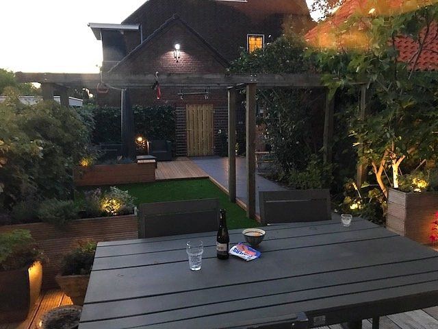 Achtertuin met een donkere tafel, drankjes en een verlichte tuin met huis.