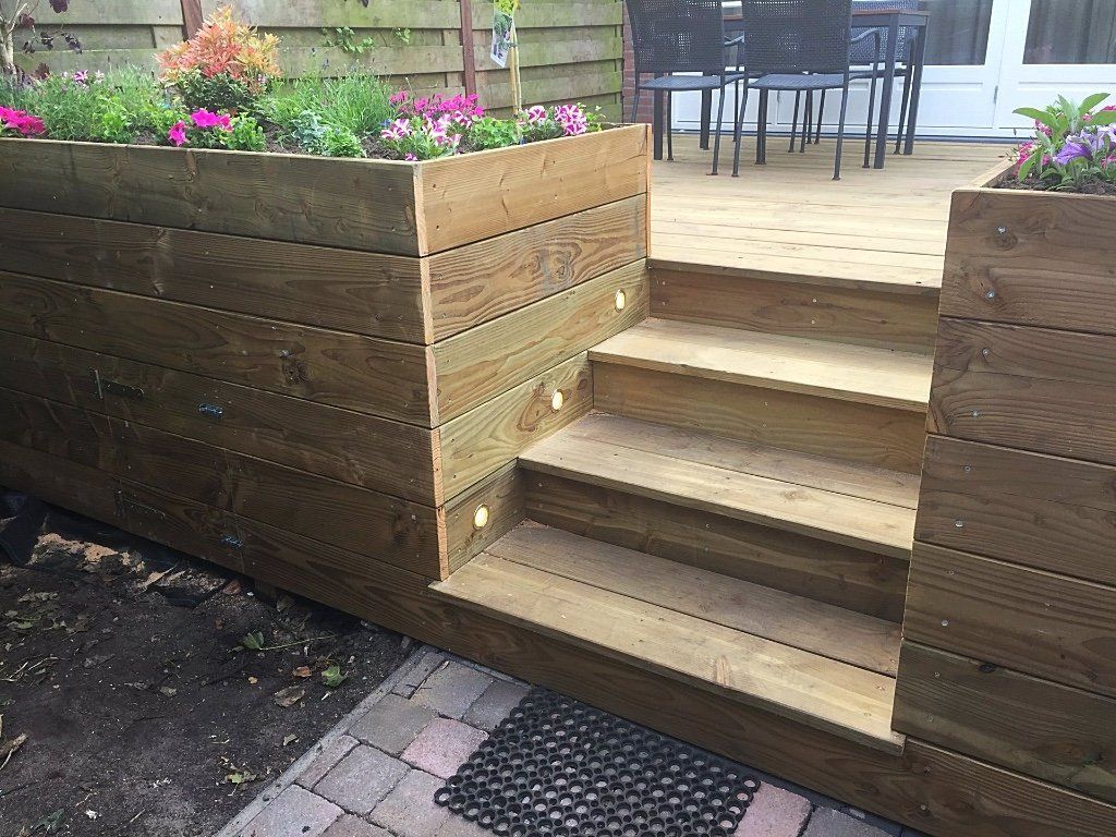 Houten plantenbak met trapjes naar een verhoogd terras. In de plantenbak staan ​​bloemen.