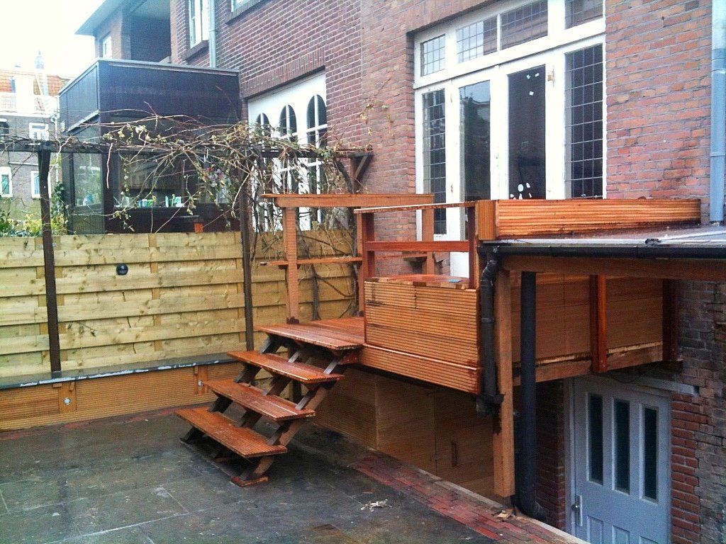 Houten terras met trap, gebouwd tegen een bakstenen gebouw.
