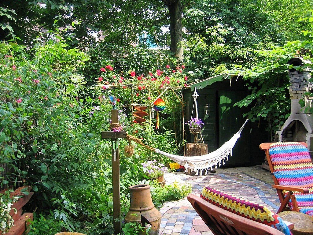 Een weelderige tuin met bloemen, een hangmat, kleurrijke stoelen en een klein schuurtje.